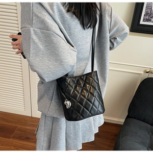Mini sac seau noir matelassé avec breloque cœur argentée porté par un mannequin chic