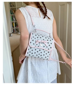 Detail eines weißen Rucksacks mit Schleifenmuster, Herzanhänger und niedlicher 3D-Schleife