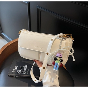 Close-up of white lychee textured bag with pearl chain and cartoon pendant on black chair