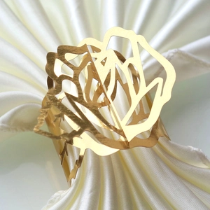 Close-up of golden hollow rose napkin ring on a white satin napkin for elegant decor