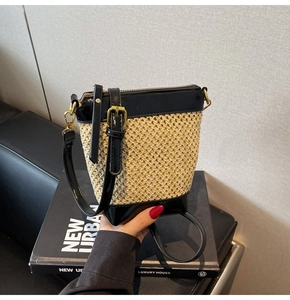 Detailed close-up of straw bucket bag featuring black leather trim and gold metal D-rings