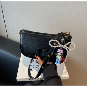 Close-up of black retro pillow bag with pearl bow charm and cartoon keychain detail