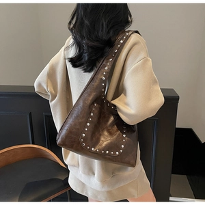 Détail d'un grand sac à main marron avec rivets porté à l'épaule par un mannequin
