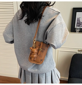 Detail showing brown vintage printed crossbody phone bag with cute bear charm