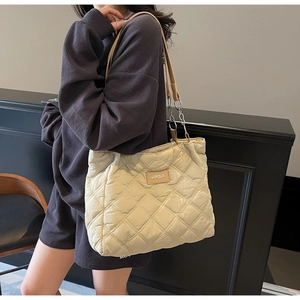 Detailansicht der beigen gesteppten Tragetasche mit Kettenriemen und Markenetikett am Outfit