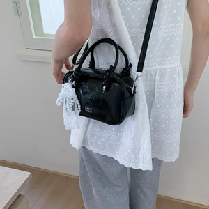 Detail einer glänzenden schwarzen Handtasche mit weißer Spitze und Perlenkette