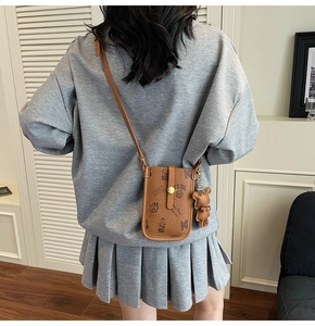 Brown leather crossbody phone bag with bear pendant shown on model in warm setting