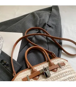 Detail of woven straw handbag featuring brown leather straps and adjustable shoulder strap