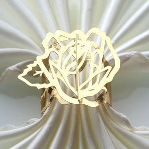Close-up of golden hollow rose napkin ring with metal floral detail on white cloth