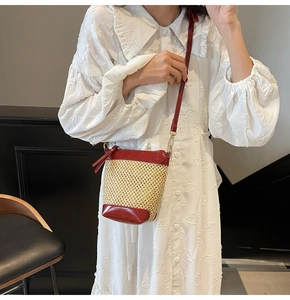 Detail view of woven straw bucket bag with red leather trim on white lace dress