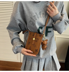 Close-up of brown textured leather phone bag featuring bear print and cute bear pendant