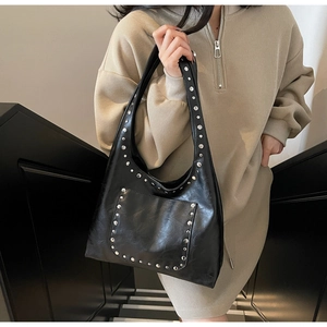 Détail d'un sac hobo en cuir noir avec clous argentés porté par un mannequin