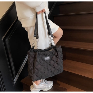 Modische schwarze gesteppte Shopper-Tasche mit Silberkette auf einer Holztreppe im Detail