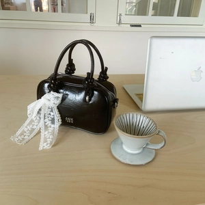Nahaufnahme einer braunen Leder-Handtasche mit weißer Spitzenschleife und Perlen
