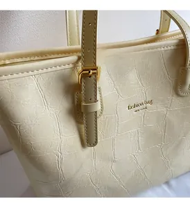 Close-up of cream tote bag featuring crocodile embossed texture and gold metal hardware
