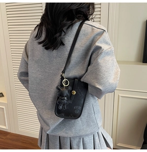 Detail of black pebbled leather crossbody phone bag with bear charm shown on model