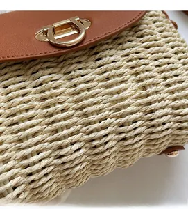 Detail of woven straw shoulder bag featuring brown leather flap and golden buckle