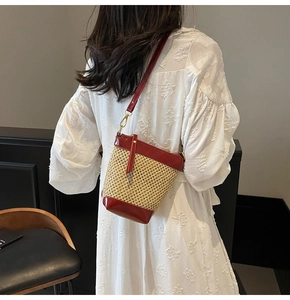 Detailed close-up of straw bucket bag with dark red leather trim and gold metal hooks