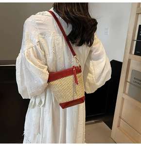 Detail of hand-woven straw bucket bag with red leather trim and shoulder strap on model