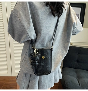 Detail view of black embossed leather phone bag with teddy bear charm and strap