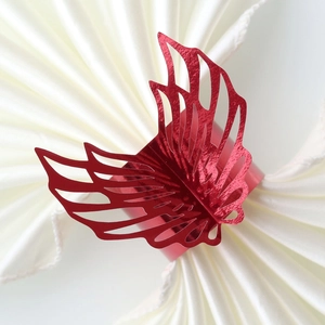 Close-up of red hollow wing napkin ring with metallic luster on white fabric