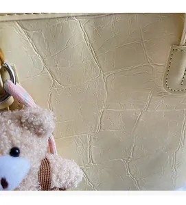 Close-up of beige crocodile pattern tote bag with logo and cute plush bear charm