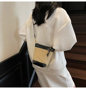 Straw bucket bag detail showing contrast black leather trim and woven texture on model
