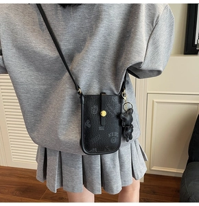 Close-up of black lychee leather crossbody phone bag with gold clasp and bear charm