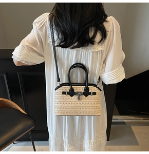 Rear view of model holding a beige woven straw bag with black leather trim and silver lock