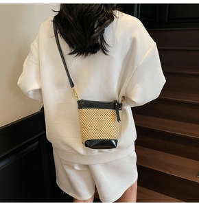 Detail of the straw bucket bag with black leather trim and golden metal hooks on strap