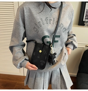 Chic black mini crossbody bag with retro logo print and cute bear charm on a model