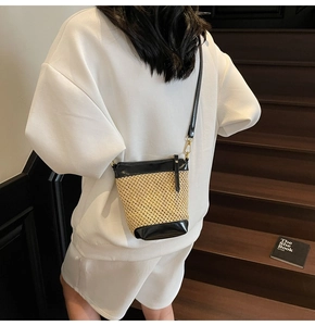 Detail of straw crossbody bag with beige woven texture and black leather trim accents