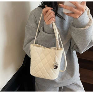 Dettaglio della borsa a secchiello trapuntata beige con manico a nodo e ciondolo argento