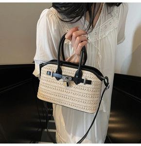 Detail of woven straw handbag with black leather trim and metal clasp worn by model