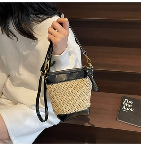 Detail of a straw bucket bag with black leather trim worn on a crossbody strap