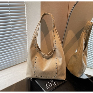 Détail du sac hobo beige avec clous argentés et texture en cuir lisse sous une lumière douce