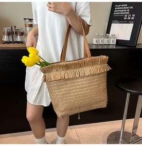 Detailed view of woven straw tote bag with fringe trim and leather handles