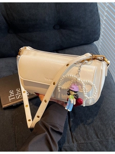 Vintage white PU leather pillow bag with pearl bow and doll charm on a sofa
