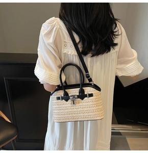 Detail view of woven straw handbag featuring black leather handles and metal lock