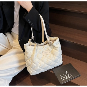 Detail einer beige gesteppten Tragetasche mit Rautenmuster und Logo auf Stufen