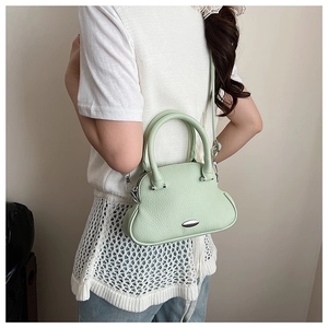 Detail showing the light green lychee leather texture and curved bottom of the shell bag