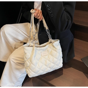 Nahaufnahme einer weißen gesteppten Shopper-Tasche mit silbernen Kettenriemen auf Holzstufen