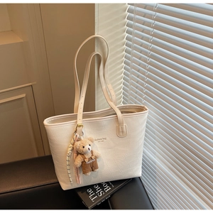 Detail of cream tote bag with crocodile texture and cute bear pendant on a dark seat
