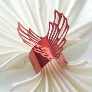 Macro detail of red laser-cut butterfly napkin ring on white satin fabric background
