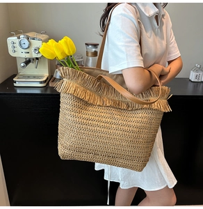 Detail of woven straw tote bag featuring decorative fringe and brown leather shoulder straps