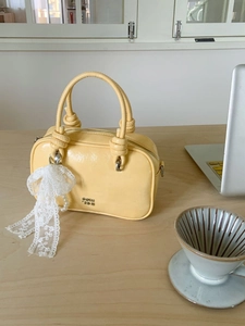 Hellgelbe Handtasche mit Falten-Optik, Spitzenbogen und Perlenkette auf dem Tisch