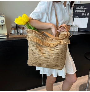 Detail of hand-woven straw tote with thick fringes and brown leather shoulder strap