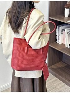 Red herringbone tote bag with small charm on model in front of a wooden bookshelf