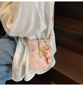 Detail of pink pebbled leather mini crossbody phone bag with embossed cartoon bear patterns