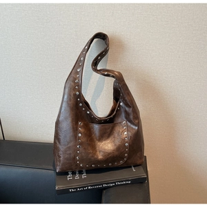 Détail d'un sac cabas marron foncé vintage avec clous argentés sur un livre élégant